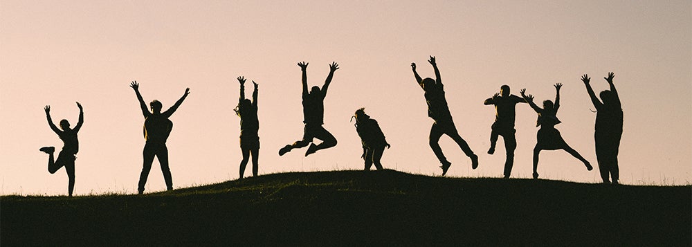 Figures in silhouette jump for joy on a hill