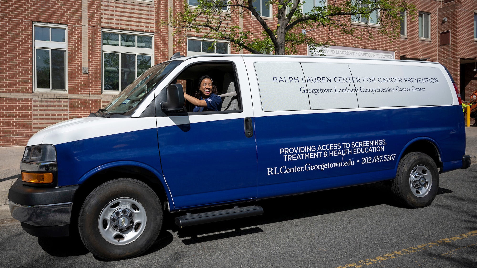 A woman drives a 12-passenger van displaying the logo of the Ralph Lauren Center for Cancer Prevention